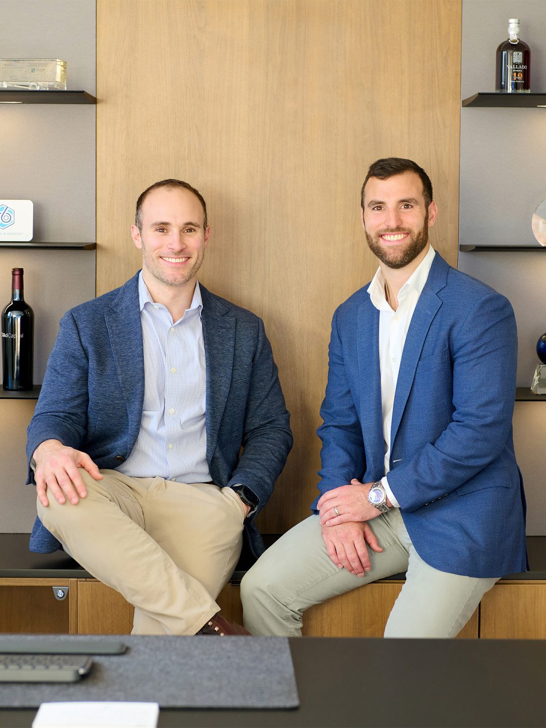 EMF Co-founders The two co-founders of Easy Mile Fitness sit on the edge of a desk and smile at the camera in an executive office.